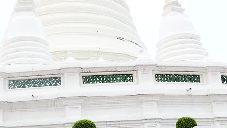 detailed view of a white pagoda with intricate latticework and manicured trees under a clear sky.