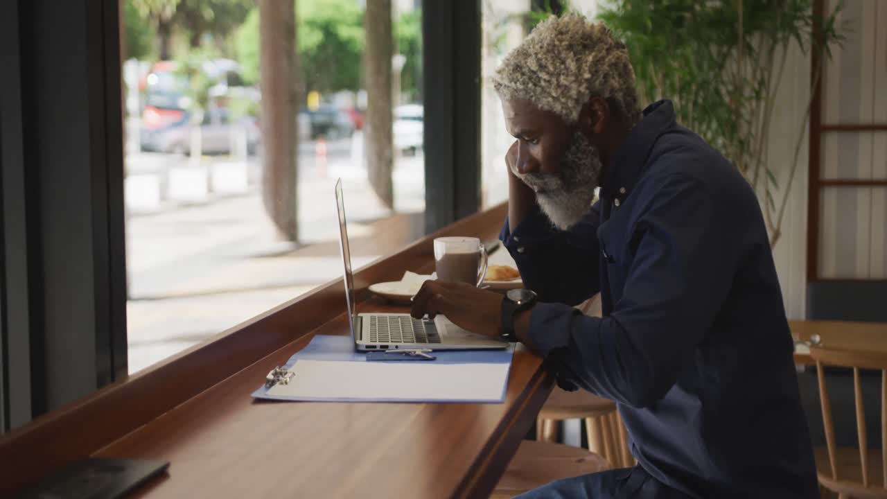 African american senior man using laptop while sitting at cafe