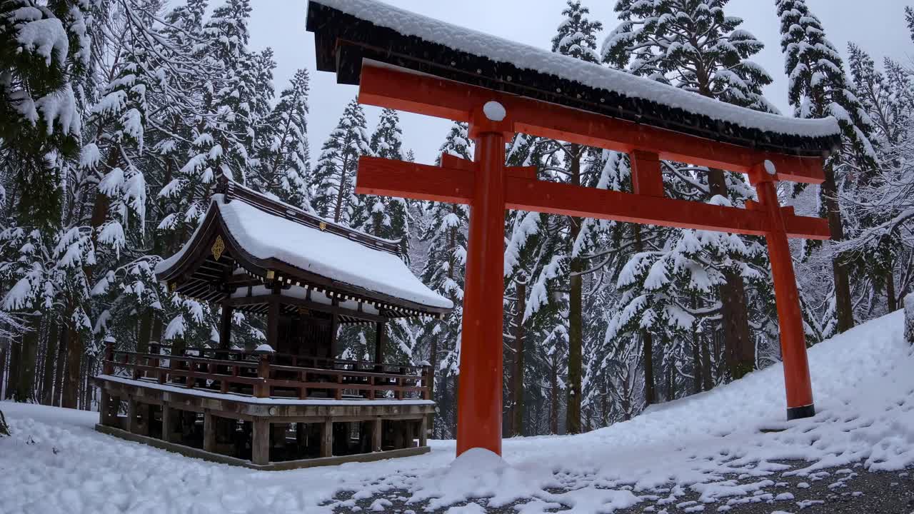 Wide-angle video frame of a snow-covered Japanese shrine and torii gate, capturing serene winter