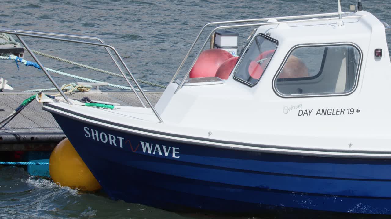 Small fishing vessel gently rocking at dock, bright daylight, calm coastal harbor, steady camera