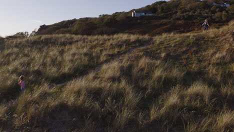 Drone-Shot-Of-Young-Girls-On-Beach-Vacation-Playing-In-Sand-Dunes-Against-Flaring-Sun