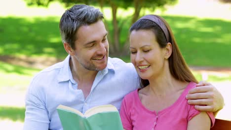 pareja sentada en un banco del parque leyendo juntos