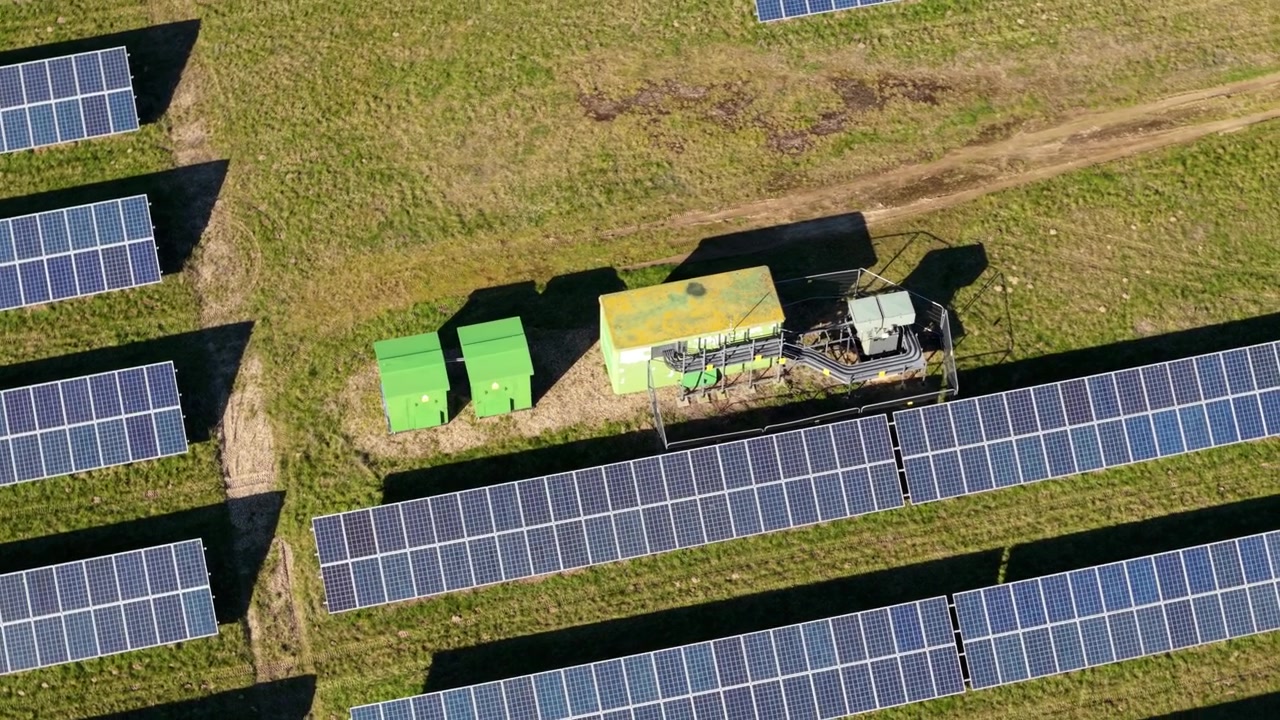 Nærbillede fra luften af solpaneler og inverter-transformerstation på en solcellepark