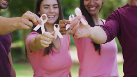 portrait of diverse group of men and women smiling and holding breast cancer ribbons in park