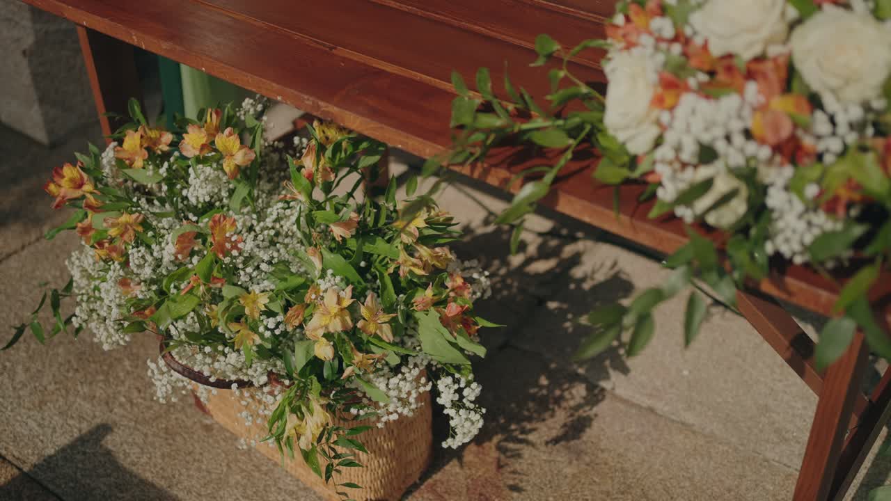 Rustic floral arrangement with white and orange flowers beside wooden bench