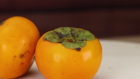 two persimmons resting on a wooden table