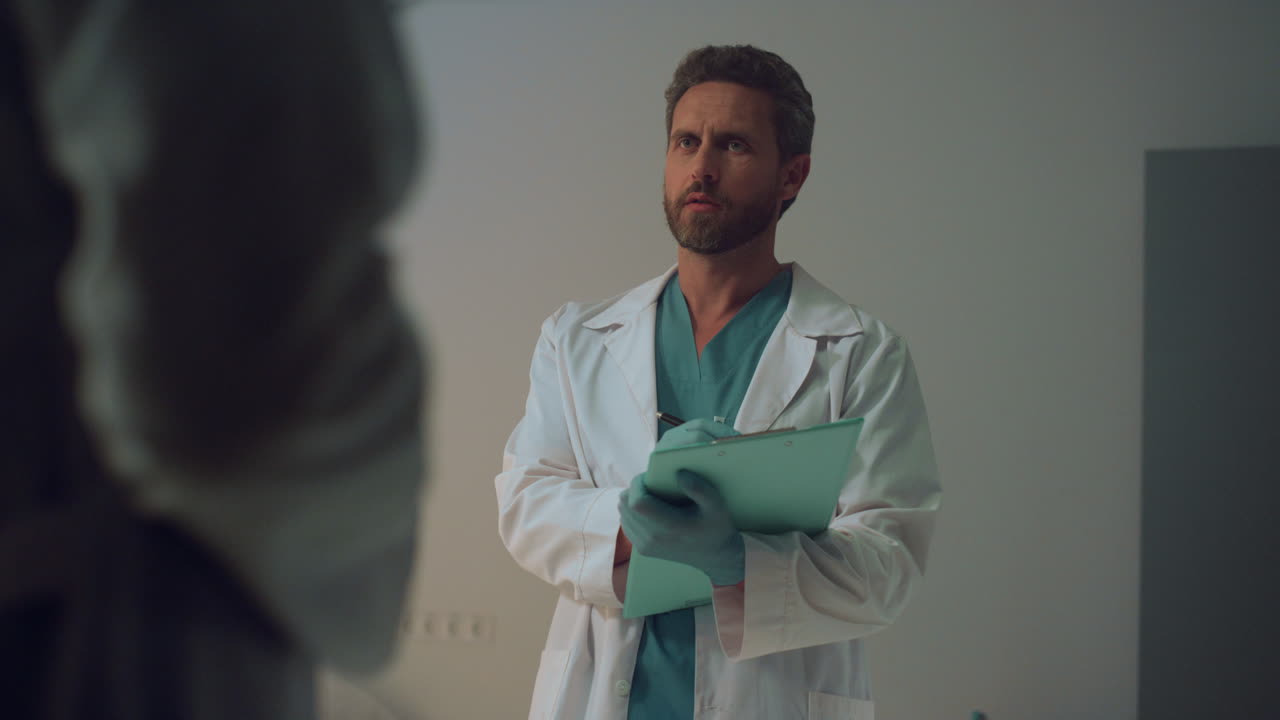 Doctors appointment in hospital ward. Serious therapist make notes on clipboard.