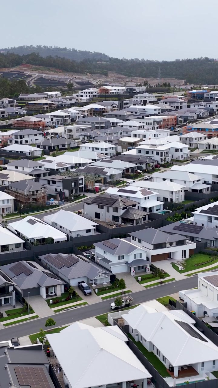 Dron deslizándose sobre casas suburbanas contemporáneas, con montañas de fondo, a la luz del día, toma amplia, movimiento constante.