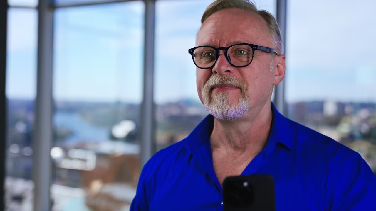 Caucasian mature bearded male in glasses talks to the phone camera. Emotional communication via smartphone. Close up.