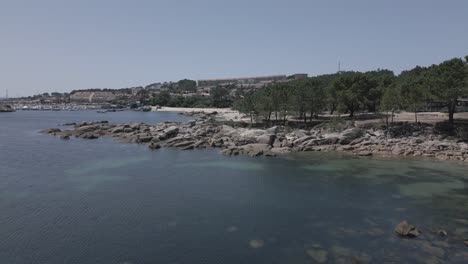 Rohe-Drohnenaufnahmen-Eines-Küstendorfes-Mit-Jachthafen-Und-Wald,-Der-Am-Strand-Endet