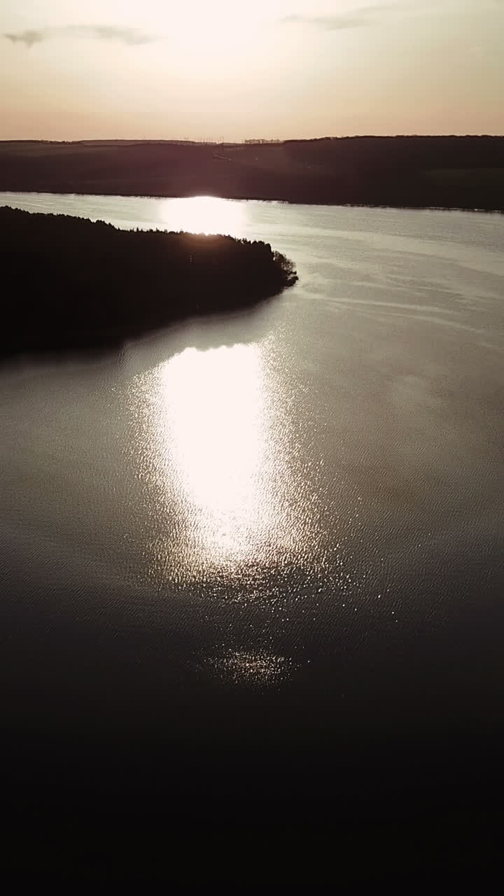 wide river is flowing at sunset in the summer. Sun's rays are reflecting in the water of the lake. Aerial view Vertical video
