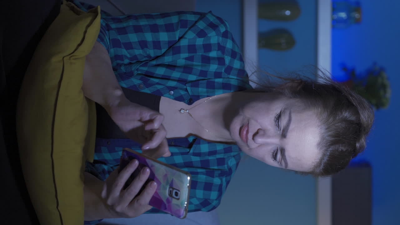 video vertical de una mujer deprimida en la noche enviando mensajes de texto por teléfono.