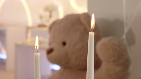 two lit candles with soft focus on teddy bear in cozy indoor setting