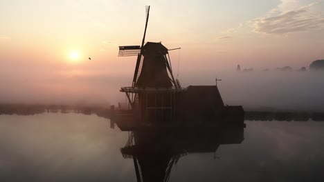 El-Dron-Vuela-Alrededor-De-Un-Molino-De-Viento-Con-El-Sol-Saliendo-Revelando-Detrás-Del-Molino-De-Viento-Y-Mucha-Niebla-En-De-Zaanse-Schans,-Imágenes-Aéreas-De-Los-Países-Bajos-4k