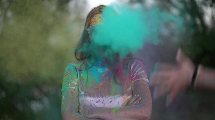 Portrait of woman standing being covered in coloured powder at holi festival.