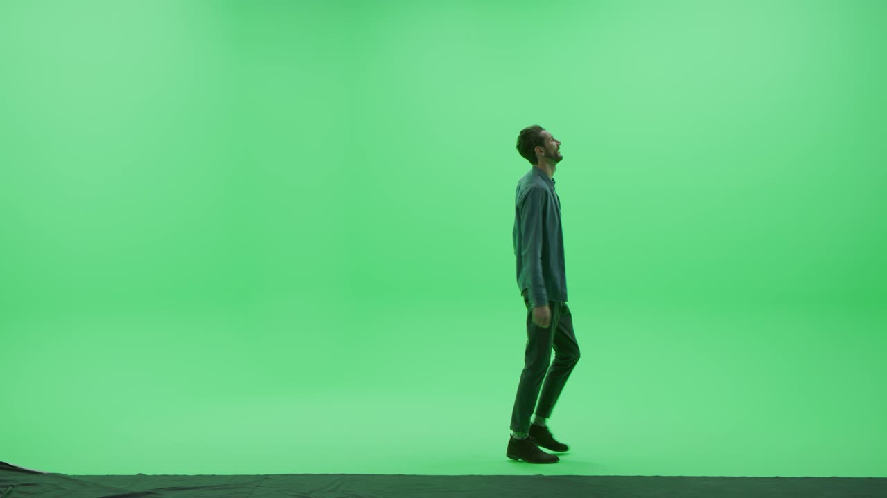 Yeşil Ekran Chroma Key Stüdyosu: Günlük kıyafetli, güçlü, yakışıklı, gülümseyen adam odada soldan sağa dans ediyor. Yan kamera çekimi.