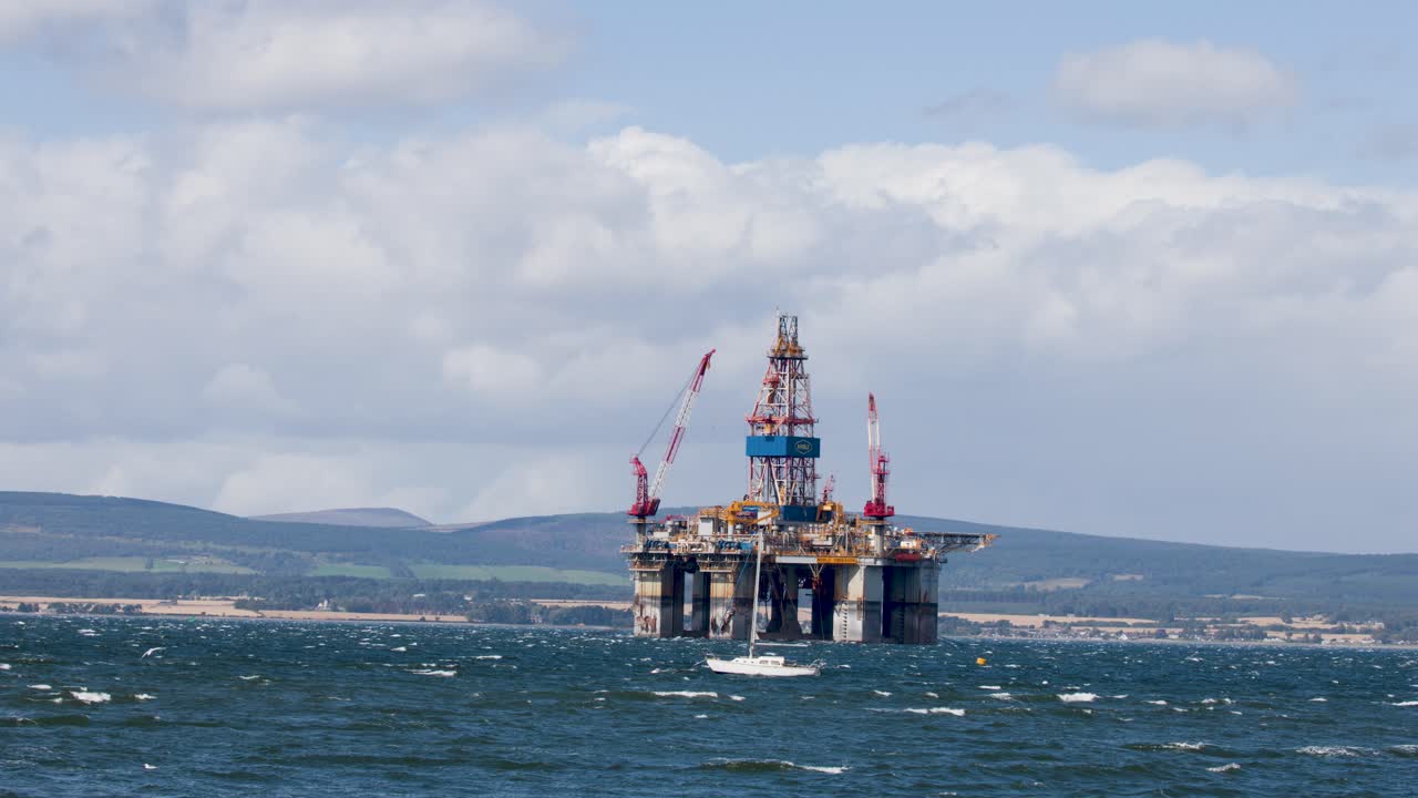 Offshore oil platform and passing yacht in daylight, wide shot, steady camera, Cromarty, Scotland