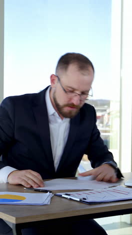 nervous businessman in office. irritated man entrepreneur sitting at table and tearing papers throwing them to the sides on the background of window. vertical video