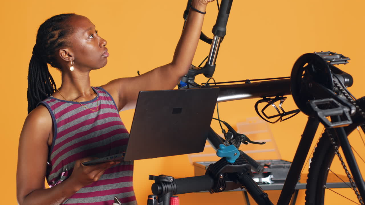 Engineer does bike servicing, looking on laptop maintenance list, studio background