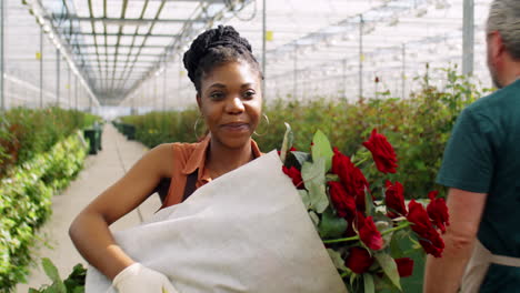 mujer afroamericana caminando con rosas en un invernadero de flores