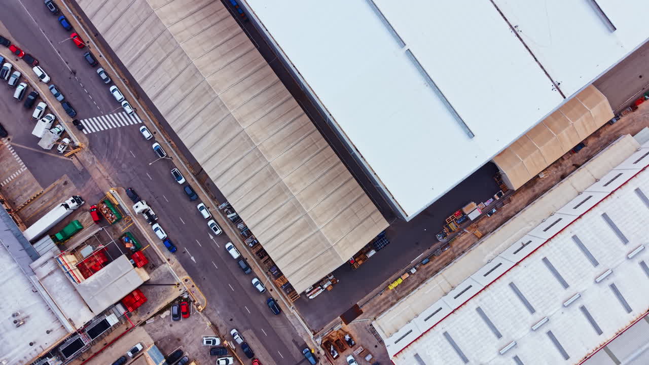 Udsigt over en travl gade i et industriområde med parkerede biler og varehuse i dagtimerne, der viser organiseret kaos