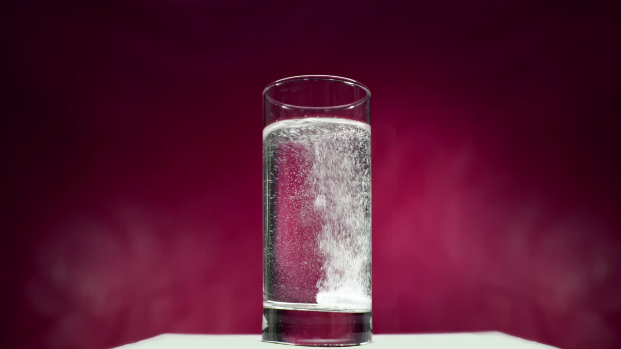 vaso de agua con comprimido blanco disolvente sobre fondo rojo