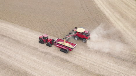 combine harvester collecting grain crops and transferring into grain cart attached to tractor, aerial