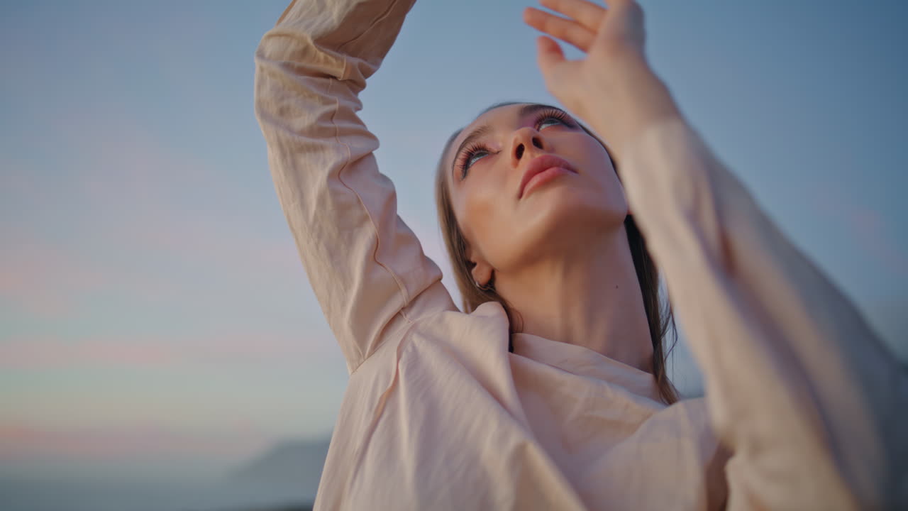 가까운 여자아이가 해가 지는 앞 하늘에서 감각적으로 팔을 춤추고 여자 손을 움직인다