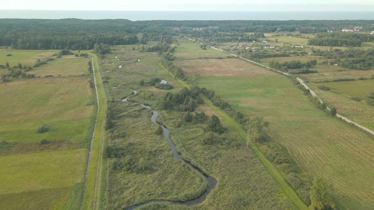 Aerial slow forward movement over farms and green fields of Debki village in Poland, drone flying straight