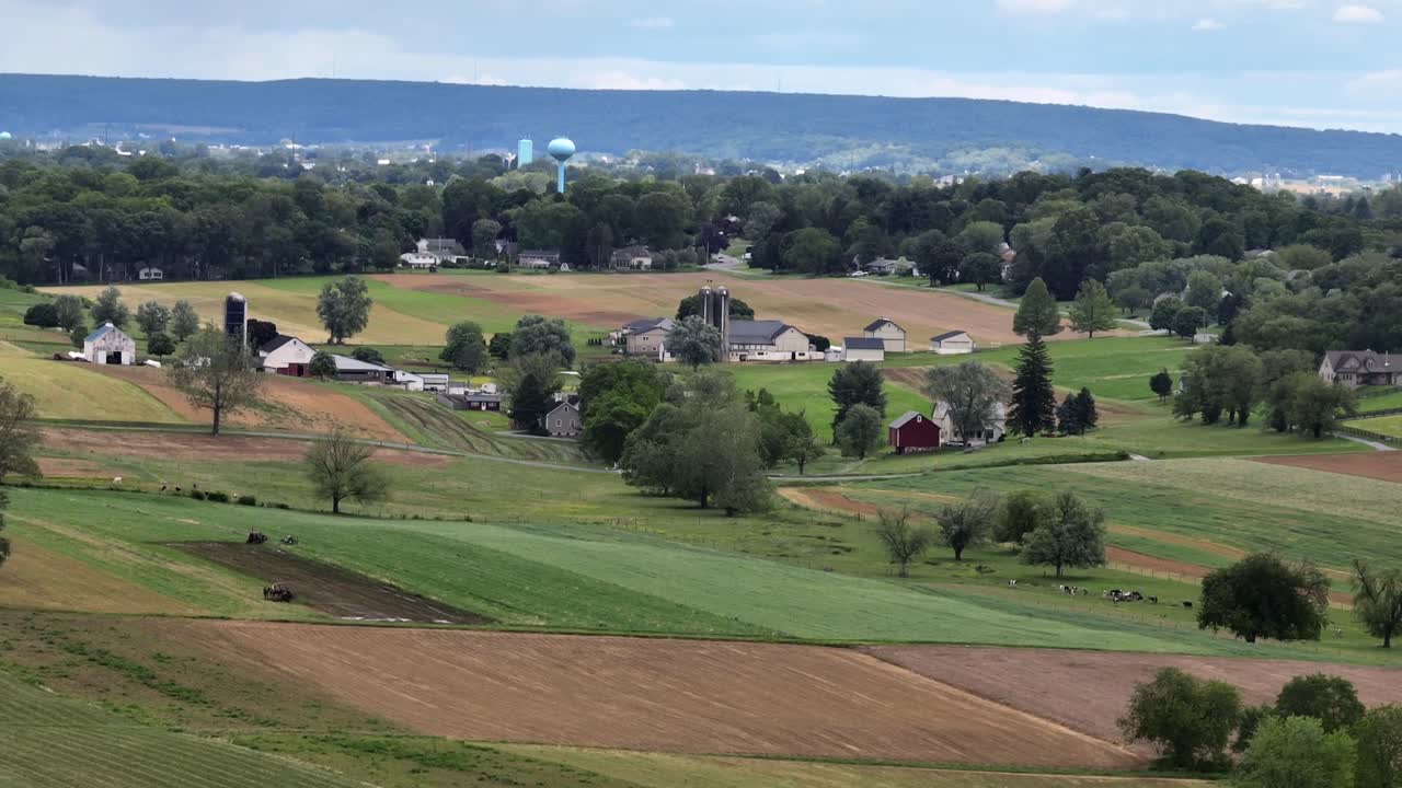 Hilly farm fields in rural area of American town. Aerial wide shot. Sunny day with farmers house and barn in distance. Aerial wide shot. Pennsylvanian countryside fields