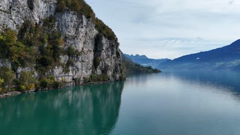 a stunning turquoise lake at the foot of a steep cliff with beautiful blue hazy mountains in the distance