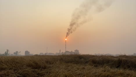 Gas-plant-tower-flame-polluting-air,-sunset-matching-tower-top,-handheld