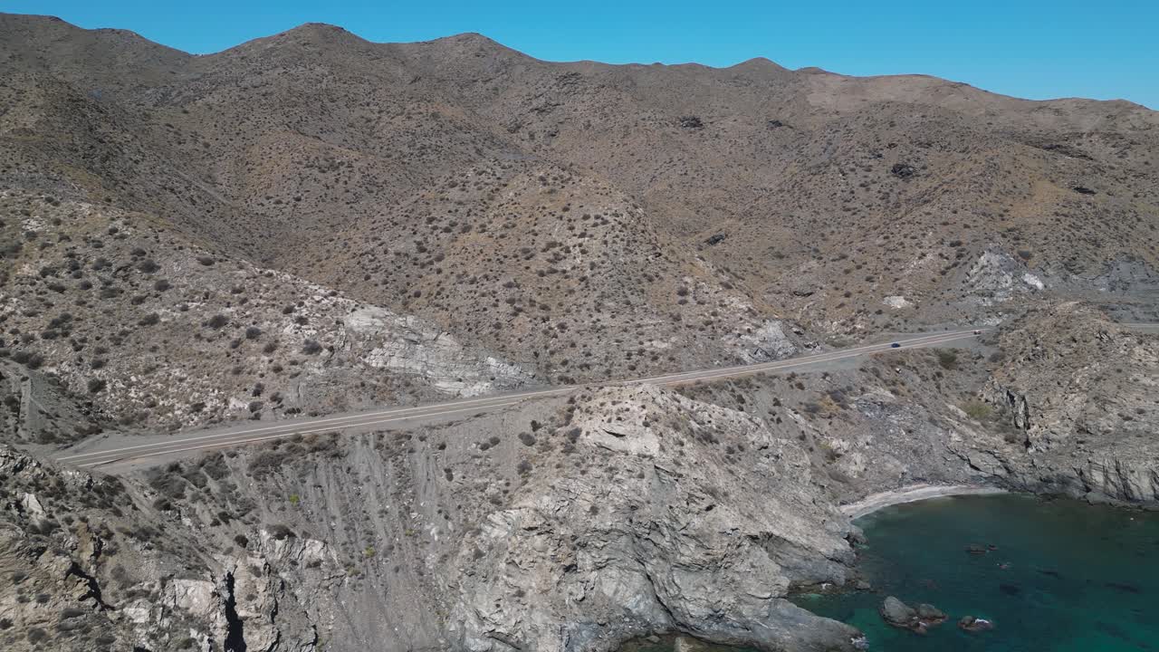 Aerial view of a winding coastal road along the rugged shoreline near Almería in the Andalusia region of Spain, with cliffs dropping to the blue Mediterranean Sea