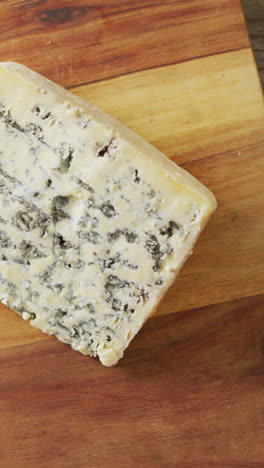 video overhead shot of wedge of blue cheese on chopping board, on rustic wooden table