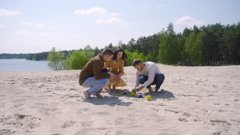 grupo de jóvenes amigos caucásicos recogiendo bolas de petanca de la arena en la playa en un día soleado