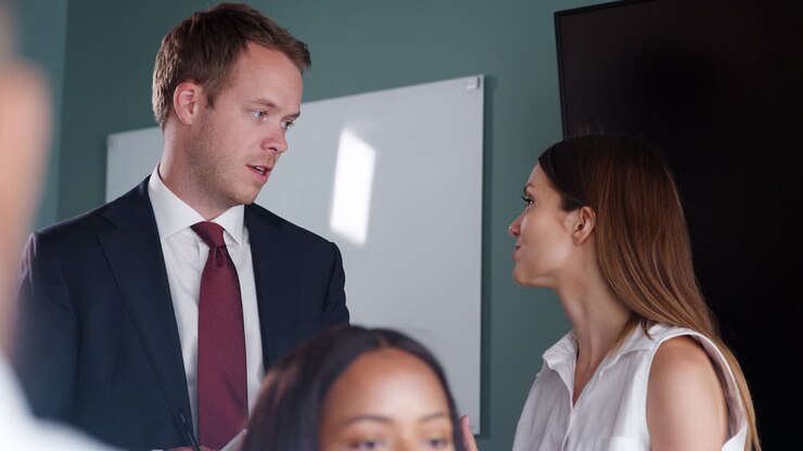 Young Businessman And Businesswoman Watching Group Meeting Around Table At Graduate Recruitment Assessment Day