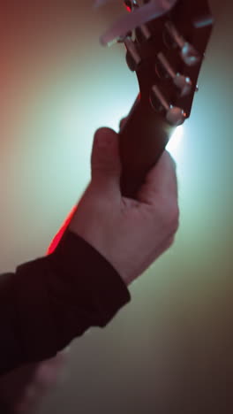 primer plano dramático de una mano tocando una guitarra roja, resaltado por una iluminación de colores vibrantes en una habitación oscura