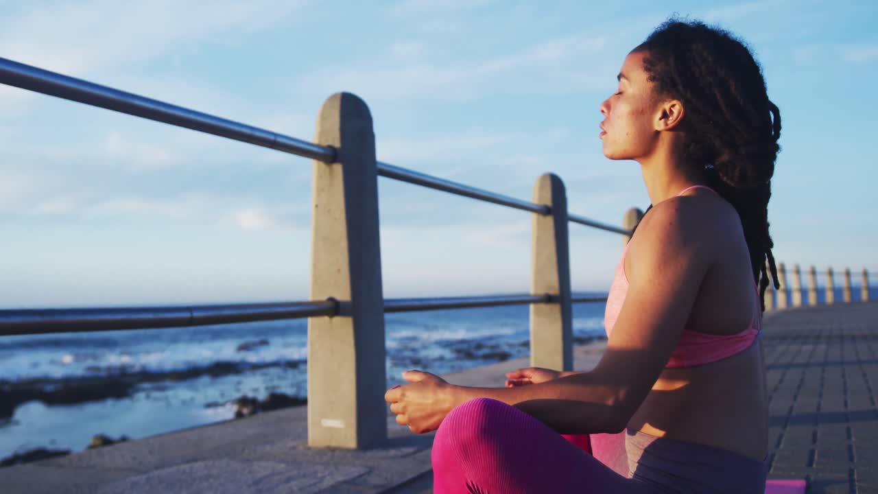 mujer afroamericana practicando yoga en el paseo marítimo cerca del mar