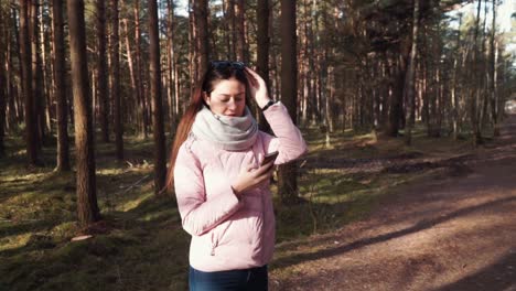 Young-female-is-standing-in-the-middle-of-forest-with-the-mobile-phone