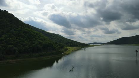 reverse aerial footage leaning next to the hill covered with trees revealing the lake and the lovely horizon and rainclouds, muak klek, saraburi, thailand