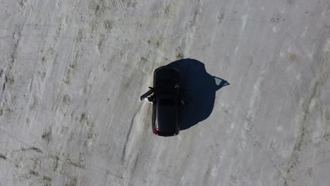 two people get into a suv, which was parked on the bonneville salt flats in utah on a summer day. aerial drone shot directly from above the car, showing tire tracks and shadows. 4k cinematic footage.