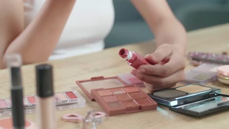 female hands holding lip gloss on the vanity and using it for applying makeup at home