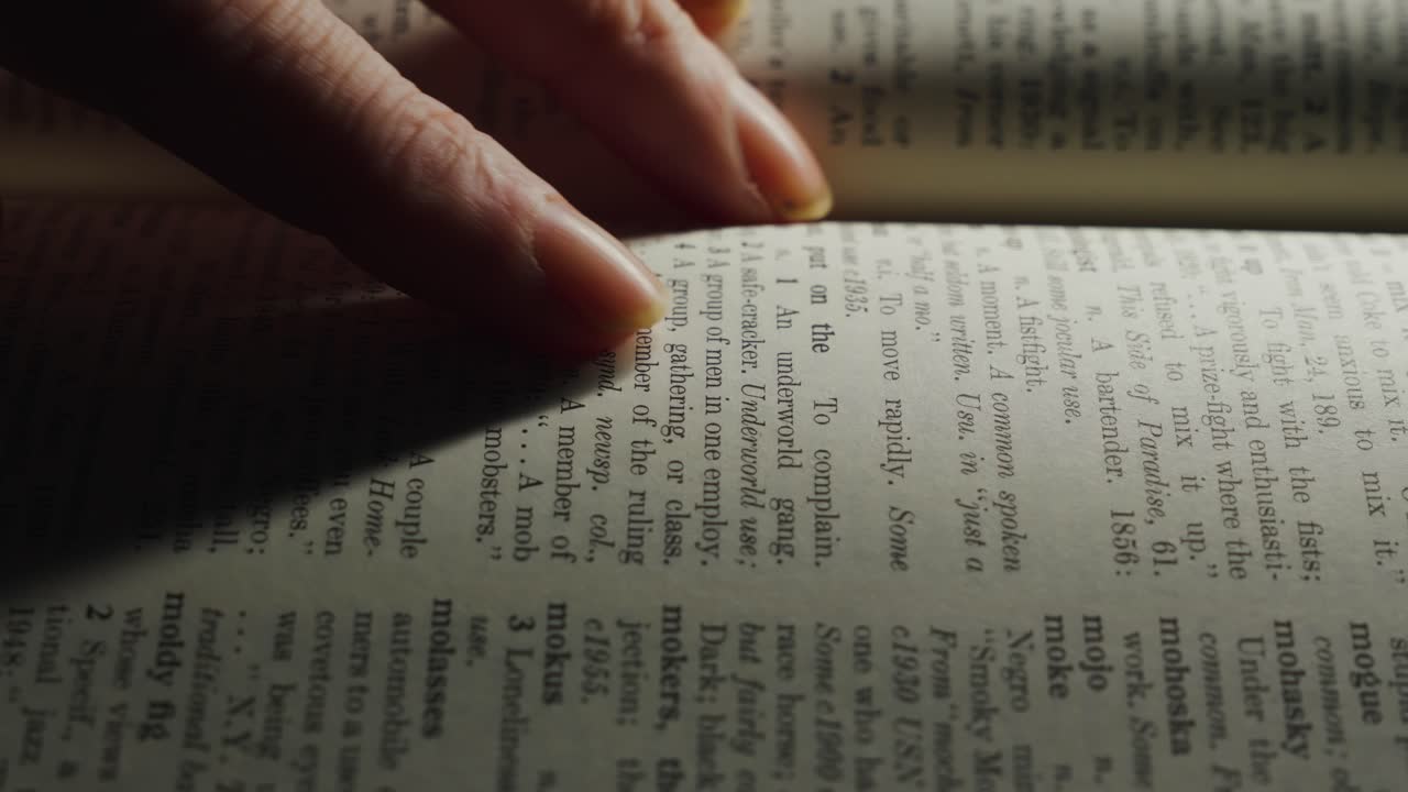 Close-up of a hand turning the pages of a book, with the text on the page partially visible