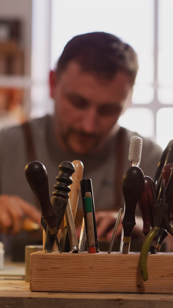 Hand of master takes cutter to process leather from wooden rack on workbench closeup. Manual tools of craftsman in workshop. Traditional industry