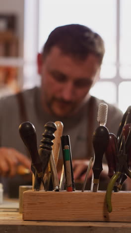 hand of master takes cutter to process leather from wooden rack on workbench closeup. manual tools of craftsman in workshop. traditional industry