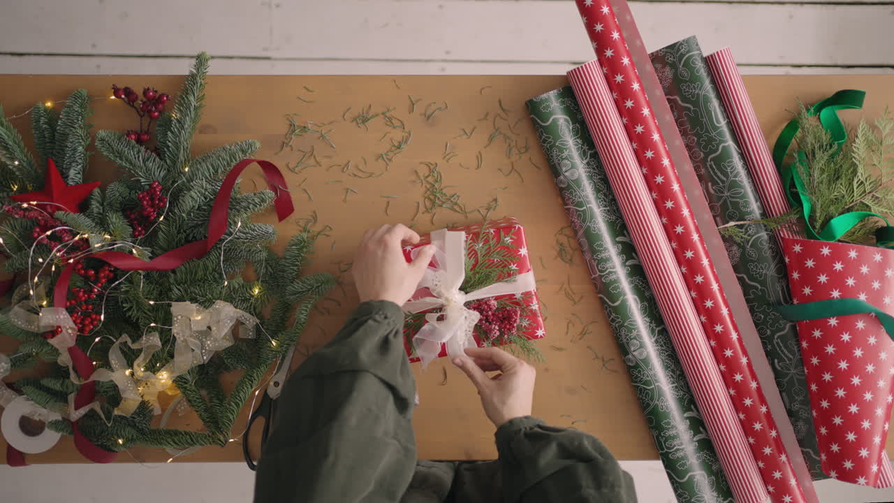 plan de arriba hacia abajo: una mujer pone un regalo sobre la mesa para envolverlo y le aprieta una cinta de regalo. mesa decoradora y envoltorio de regalos