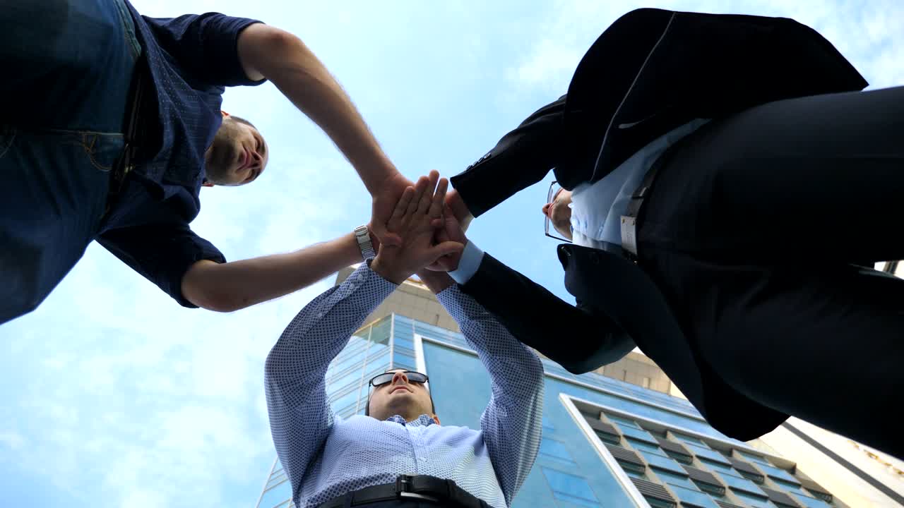 Three business men standing outdoor near office and stacked arm together in unity and teamwork. Hands of business partners get together in the center of a circle and then raised. Low angle of view Close up Slow motion