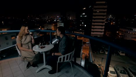 man and woman having drinks on the rooftop cafe in night city