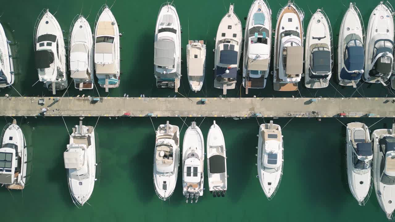 Boats docked at a marina, with clear turquoise water, aerial view