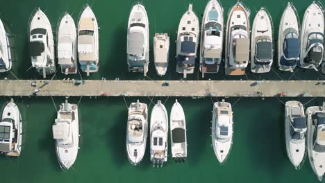 Boats-docked-at-a-marina,-with-clear-turquoise-water,-aerial-view